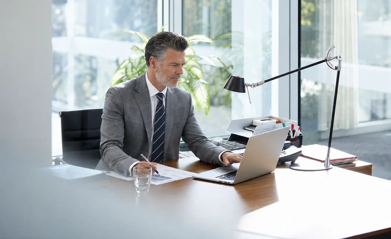 An auditor at his desk, pen on the findings letter, laptop open.